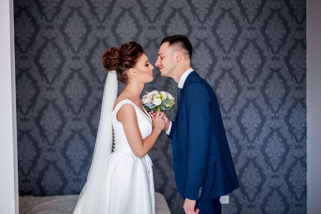 Belle Mariée En Robe Blanche Avec Bouquet De Mariées Et Beau Marié En Costume Bleu Debout à La Maison à La Maison