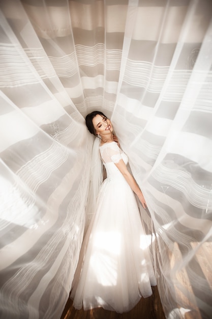 Belle mariée en robe blanche posant sous le rideau