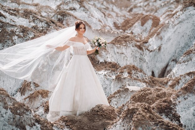 Belle mariée en robe de mariée avec un bouquet au sommet des montagnes de sel. Une superbe jeune mariée aux cheveux bouclés. Jour de mariage. . Beau portrait de la mariée sans le marié.