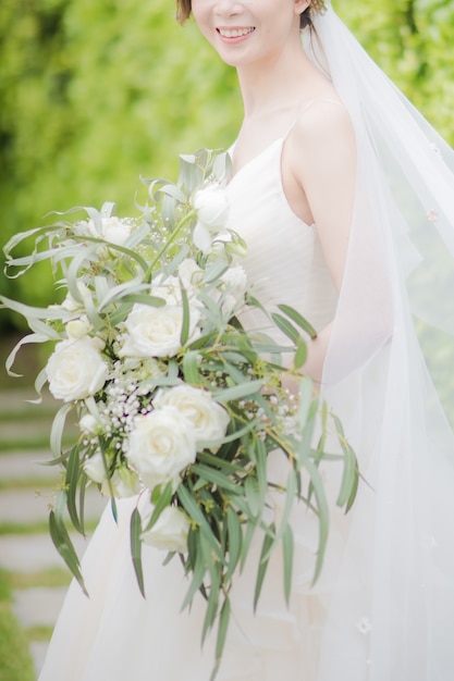 Belle mariée en robe de mariée sourit joyeusement et tient un bouquet de fleurs