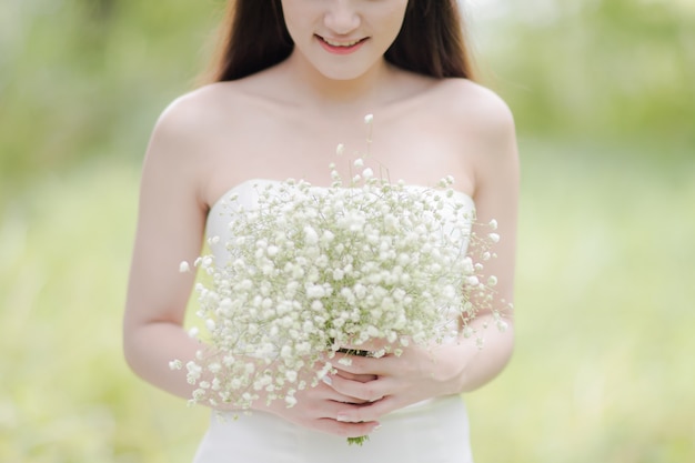 Belle mariée en robe de mariée sourit joyeusement et tient un bouquet de fleurs