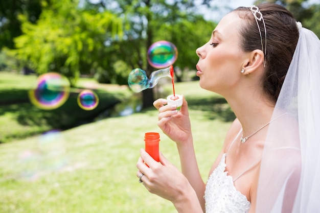 Belle mariée soufflant des bulles dans le jardin