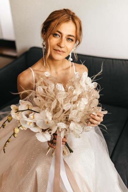 Photo belle mariée souriante avec un bouquet dans les mains dans une robe de mariée blanche dans un studio loft