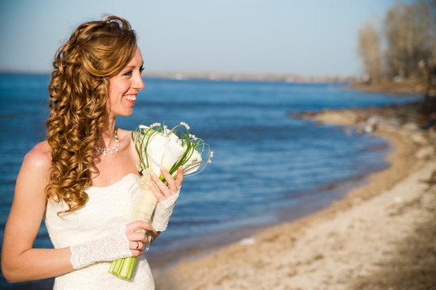 Belle mariée vêtue d'une robe blanche sur la côte de la rivière en été Maquillage et coiffure professionnels