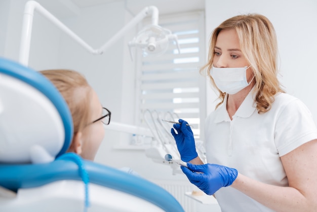 Belle médecin expérimentée attentive à la recherche de concentration tout en commençant un examen régulier des dents de ses patients