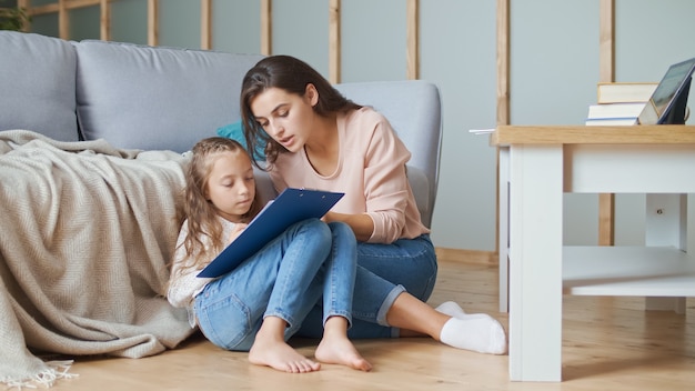 Une belle mère aide sa fille joyeuse à faire ses devoirs.