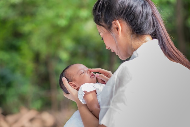 La belle mère asiatique embrasse son bébé pendant que la mère endormie montre l'amour au nouveau-né