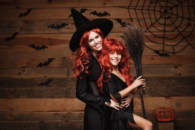 Belle mère caucasienne et sa fille avec de longs cheveux roux en costumes de sorcière célébrant Halloween posant