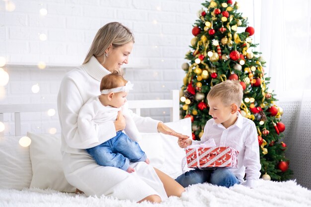belle mère avec deux enfants offre des cadeaux du Nouvel An à la maison sous le sapin pour fêter Noël