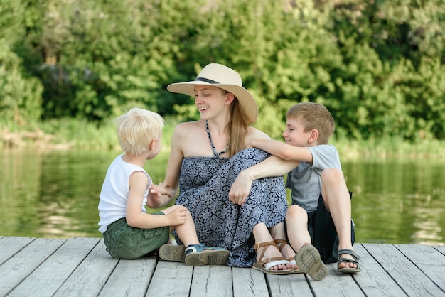 Belle mère avec deux jeunes fils sont assis sur la jetée sur la rive du fleuve.