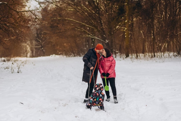 Une belle mère de famille, père et fille, monte un traîneau un jour enneigé sur fond de forêt enneigée Avant Noël et le Nouvel An en s'amusant Photo de haute qualité