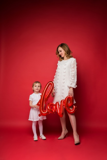 Belle mère et fille debout tenant un ballon avec l'inscription amour sur un rouge