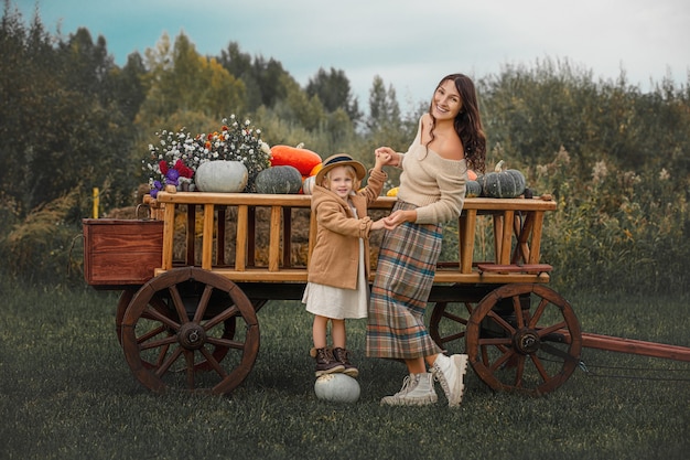 Belle mère et fille de famille heureuse ensemble sur un chariot en bois avec des citrouilles colorées