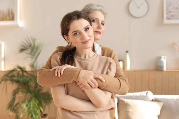 Belle mère et fille. Une jeune femme joyeuse embrasse sa mère d'âge moyen dans le salon. Portrait de famille.