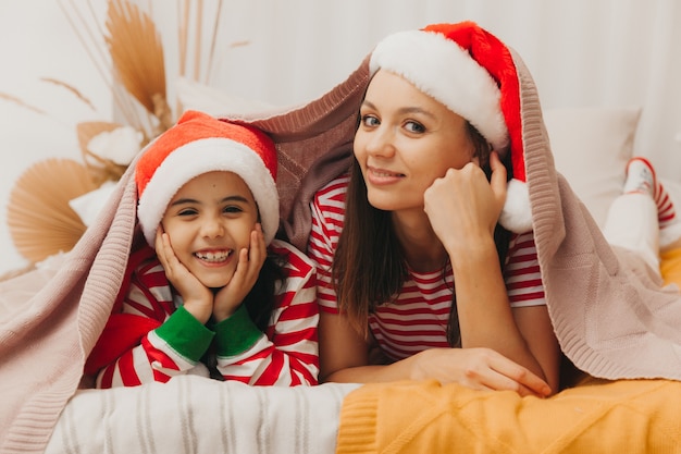 Belle mère et fille en pyjama de Noël s'embrassent et jouent à la maison dans la chambre sur le lit. Noël