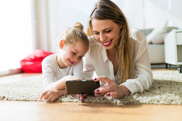 Belle mère et fille qui jouent avec un téléphone mobile à la maison.