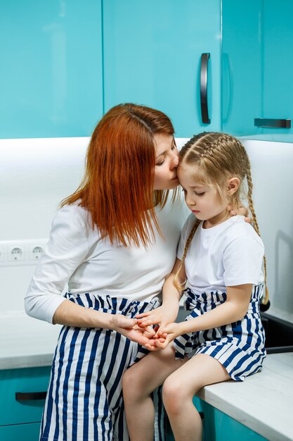 Belle mère et fille s'embrassent et sourient joyeusement, assises dans la cuisine. Concept de famille, d'enfants, de maternité et de cuisine. Relations familiales heureuses