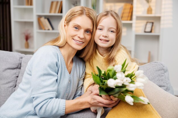 Belle mère et fille tenant un bouquet ils sont assis ensemble sur le canapé dans le salon