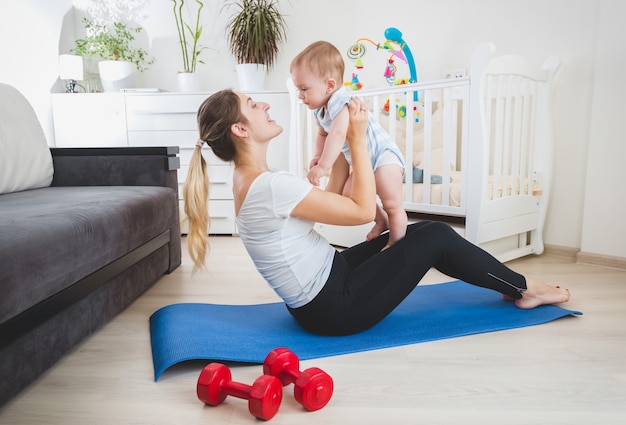 Belle mère mince jouant avec son bébé sur un tapis de fitness à la maison