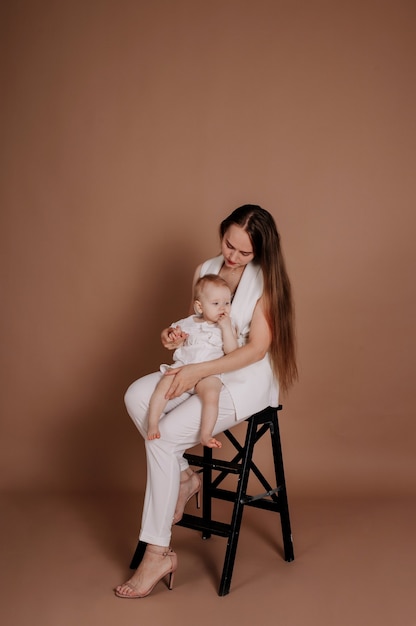 Belle mère et petite fille sont assises sur une chaise noire sur fond beige avec une place pour le texte