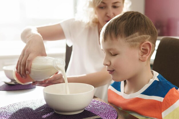 Belle mère et son fils mignon mangeant des cornflakes sains pour le petit déjeuner le matin ensoleillé