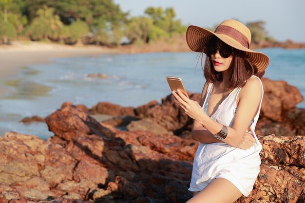 Belle et mignonne femme d'affaires à l'aide de téléphone portable avec des lunettes de soleil et un chapeau sur la plage