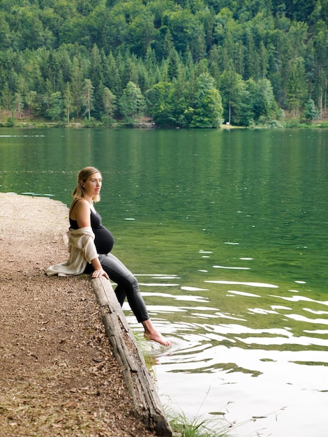 Belle et mignonne femme enceinte est assise près d'un lac de montagne dans une forêt sur la rive