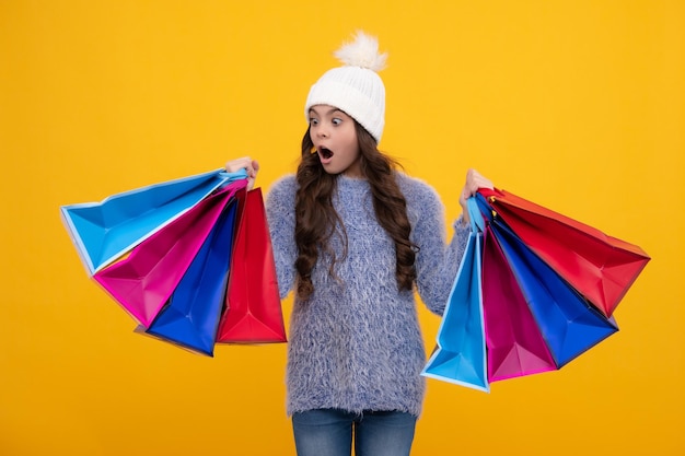 Belle mode adolescente enfant fille en chapeau chaud d'hiver avec des sacs à provisions sur fond jaune