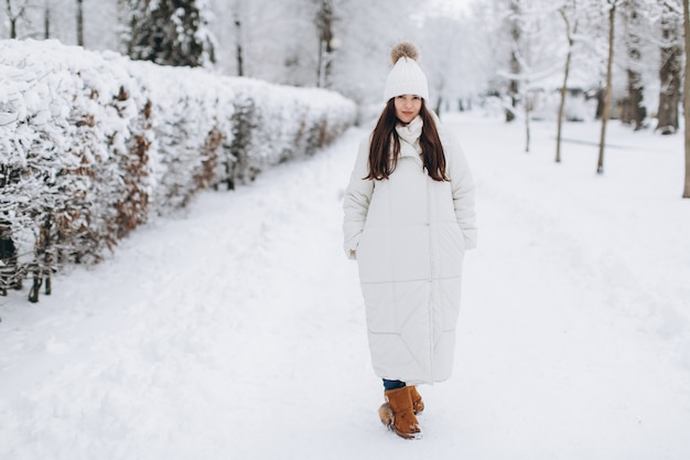 Une belle et mode femme en vêtements chauds blancs marchant dans un temps neigeux.