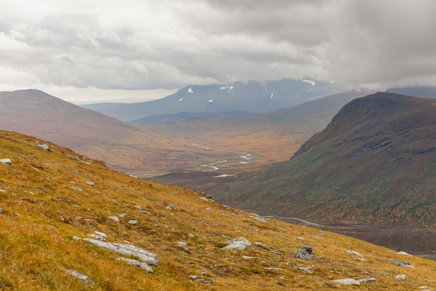 Belle nature sauvage du parc national de Sarek en Suède Laponie avec des sommets enneigés, une rivière et un lac, une forêt de bouleaux et d'épinettes. Couleurs du début de l'automne par temps orageux