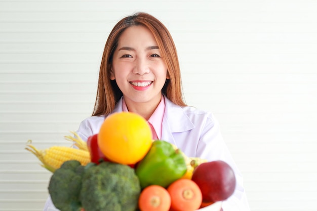 Belle nutritionniste asiatique tenant un plateau de fruits et légumes, elle a donné des conseils et préparé des aliments nutritifs Mangez des aliments sains et propres concept de soins de santé