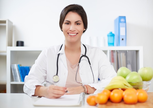 Belle nutritionniste souriant regardant la caméra et montrant des fruits sains