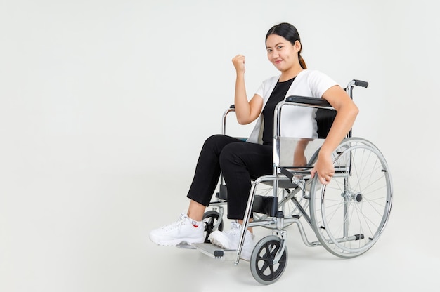 Une belle patiente montre le poing fermé et s'assoit sur un fauteuil roulant pour exprimer une bonne santé pendant la rééducation à l'hôpital. Fille asiatique handicapée confiante sur un traitement médical pour récupérer des blessures.