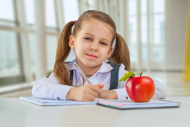 Belle petite écolière assise à table et faire ses devoirs