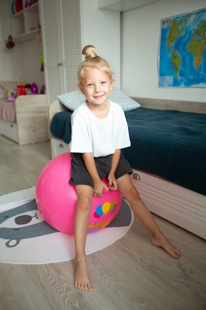 belle petite fille assise sur une balle en caoutchouc à la maison