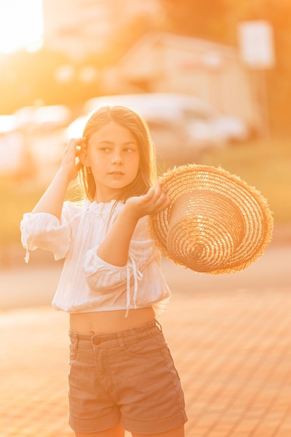 Belle petite fille au coucher du soleil dans un chapeau de paille redresse ses cheveux