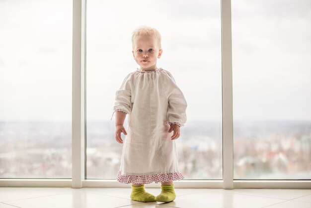 Belle petite fille aux cheveux blonds et aux yeux bleus vêtue d'un chemisier blanc et chaussettes vertes