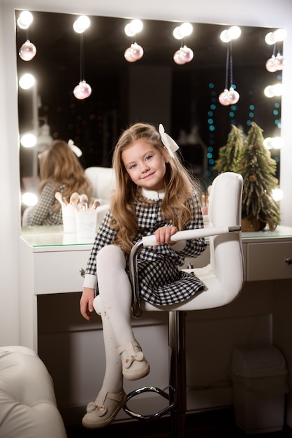 Belle petite fille aux cheveux bouclés dans un salon de beauté sur fond de grand miroir.