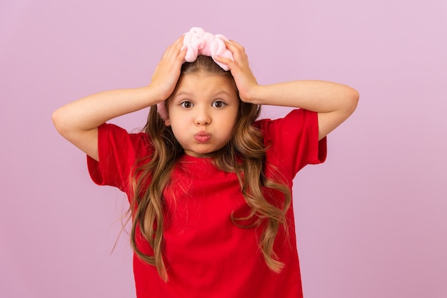 Une belle petite fille aux cheveux bouclés sur fond violet tient sa tête et gonfle ses joues.