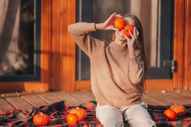 Belle petite fille aux citrouilles profitant de la journée d'automne sur la terrasse