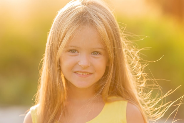 une belle petite fille aux longs cheveux blonds se promène au coucher du soleil dans le parc de la ville en été