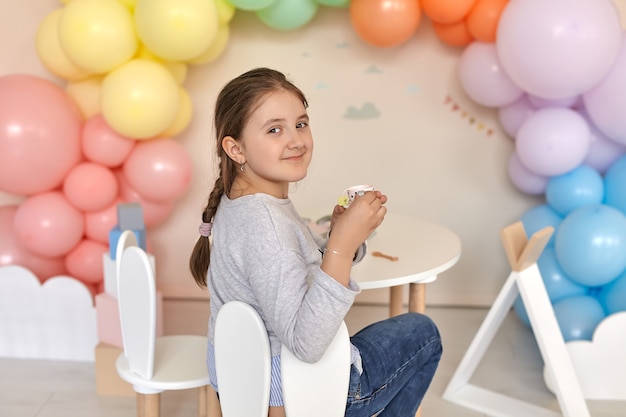 Belle petite fille ayant une tasse de thé en jouant avec un service à thé miniature dans sa chambre décorée de ballons