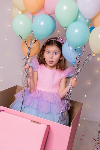 Belle petite fille avec des ballons saute d'une énorme boîte rose enfant fête son anniversaire