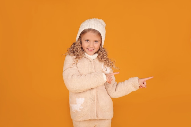 une belle petite fille blonde dans une veste tricotée et un chapeau tricoté d'hiver sur fond jaune