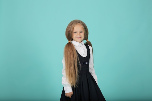 une belle petite fille blonde souriante dans une chemise blanche et une robe d'été grise est une écolière