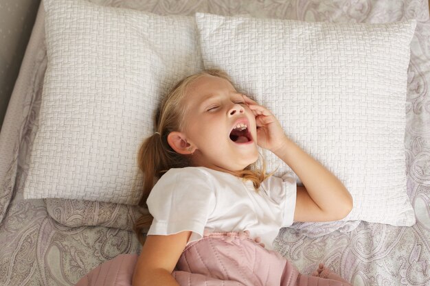 belle petite fille blonde en t-shirt blanc dort à la maison sous une couverture rose