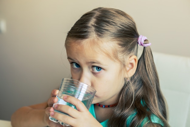 La belle petite fille boit de l'eau propre dans un verre transparent