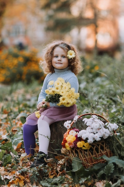 belle petite fille bouclée en chemise bleue dans le parc avec des fleurs à l'automne carte de santé d'automne