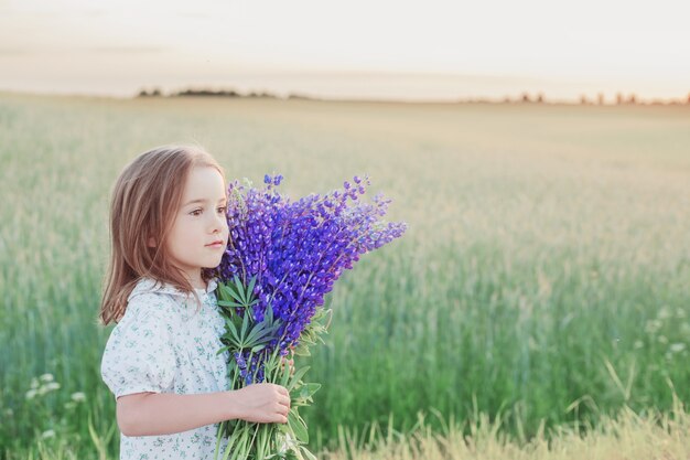 Belle petite fille avec bouquet de fleurs au coucher du soleil