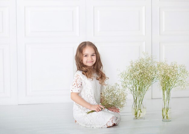 Belle petite fille avec un bouquet de Gypsophile (Baby-souffle). Portrait fille aux cheveux blonds dans une robe blanche tenant une fleurs. Bébé mignon avec un bouquet dans les mains. Le 8 mars, fête des mères